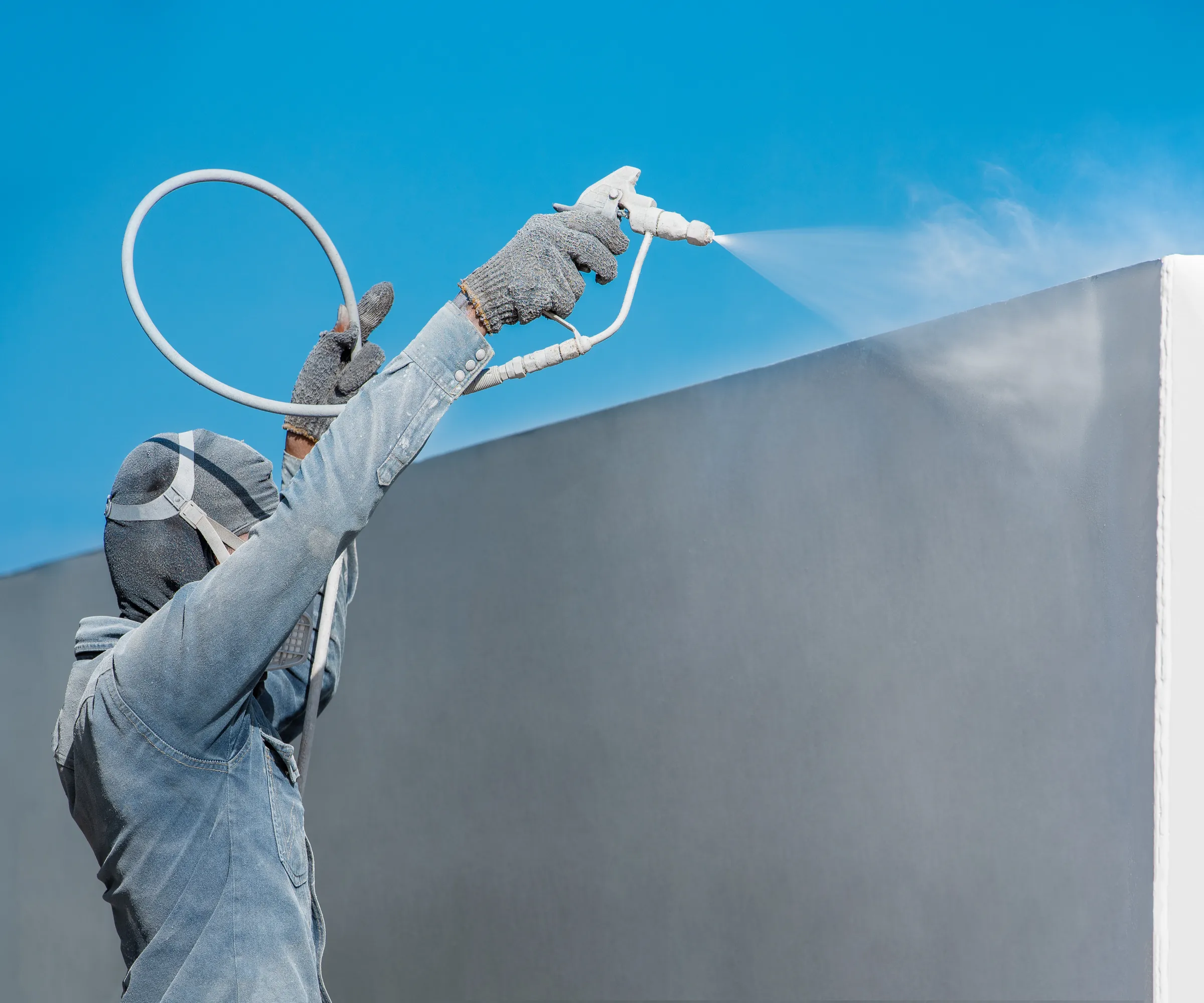 Peintre en combinaison de protection appliquant une peinture par projection Airless sur une façade