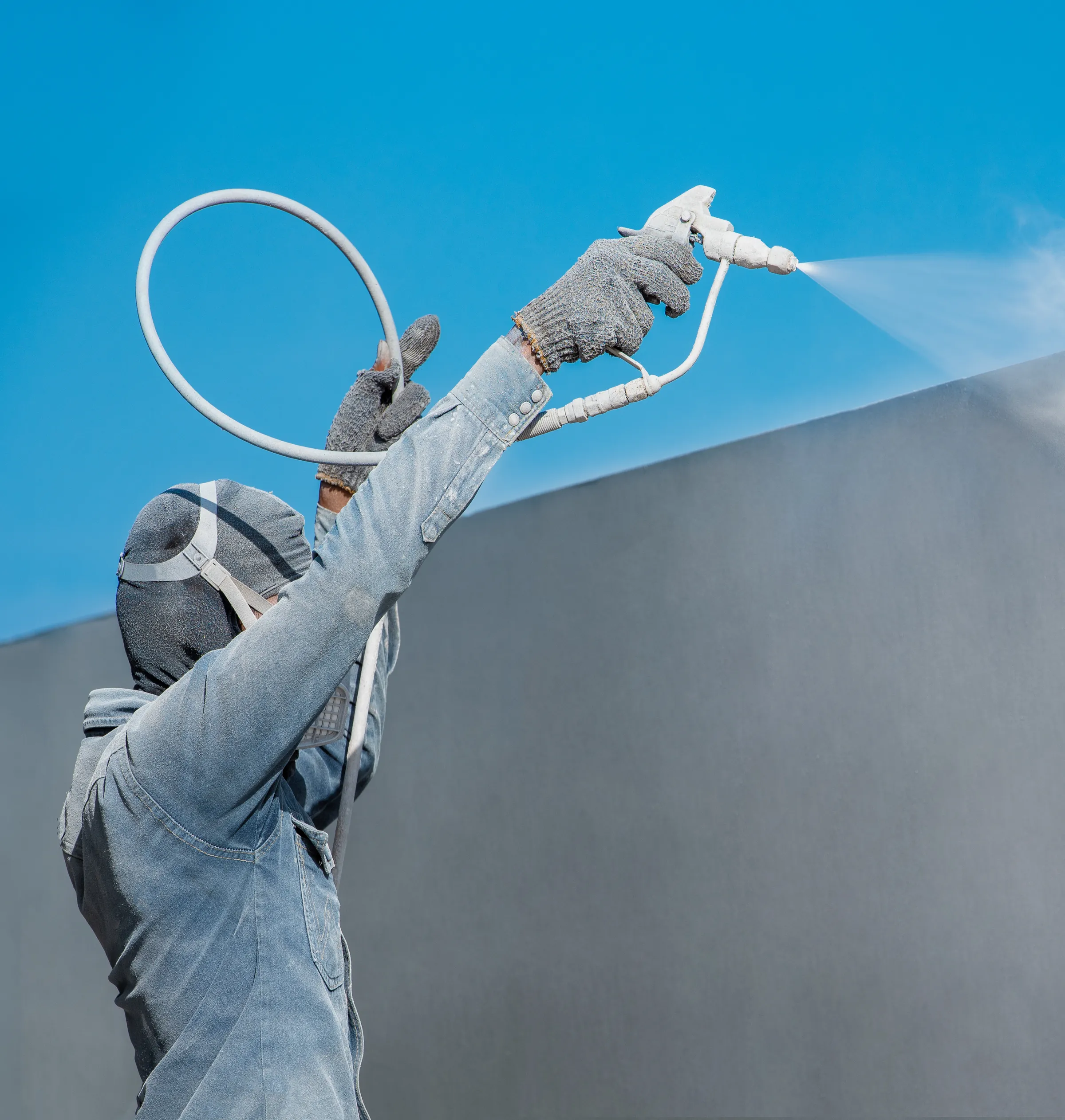 Peintre en combinaison de protection appliquant une peinture par projection Airless sur une façade