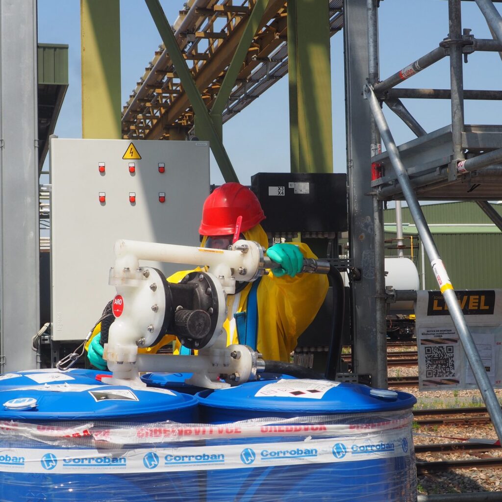 Pompe pneumatique de circulation raccordée à des fûts de réactif Corroban lors d'un nettoyage chimique sur site industriel